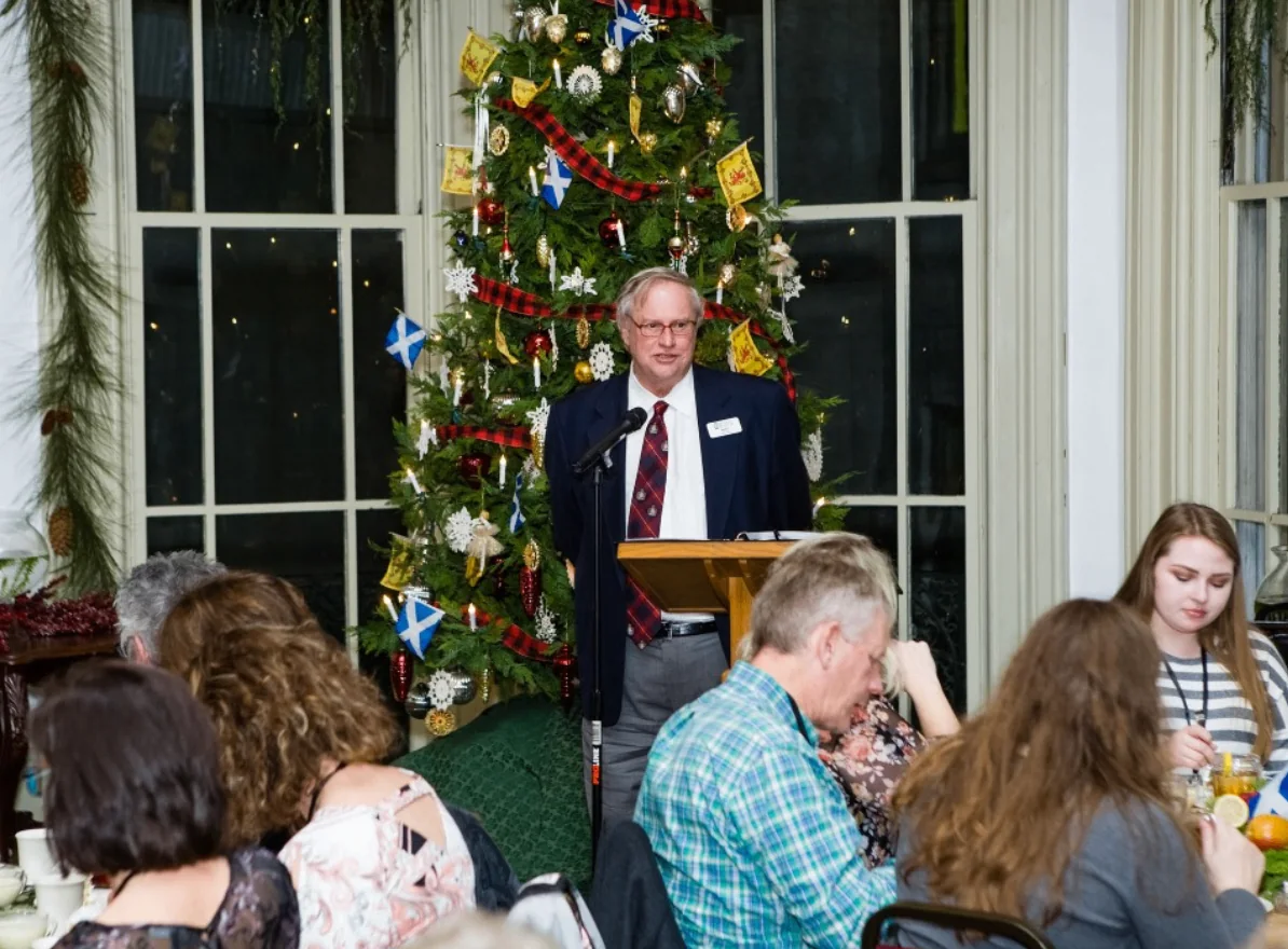 A speaker addressing Southern Mansion Reader Weekend attendees beside a decorated Christmas tree