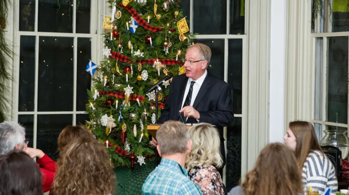 A speaker addressing guests in front of a Christmas tree during the Southern Mansion Reader Weekend