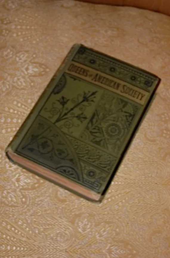 First edition copy of Queens of American Society resting on patterned fabric.
